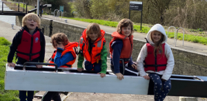 5 young people sit on a paddle of a canal lock