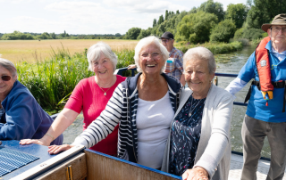 Three smiling older ladies on a canal boat with a man steering the boat behind them