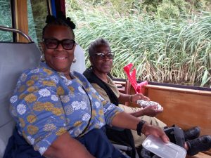 Two ladies sat inside a canal boat smiling, river and reeds can be seen in the background