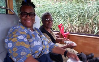 Two ladies sat inside a canal boat smiling, river and reeds can be seen in the background